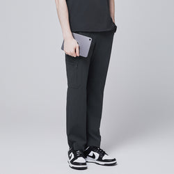 Image of Side view of deep gray straight scrub pants featuring a secure zipper pocket, modeled while holding a tablet, paired with black and white sneakers against a neutral gray background,Deep Gray