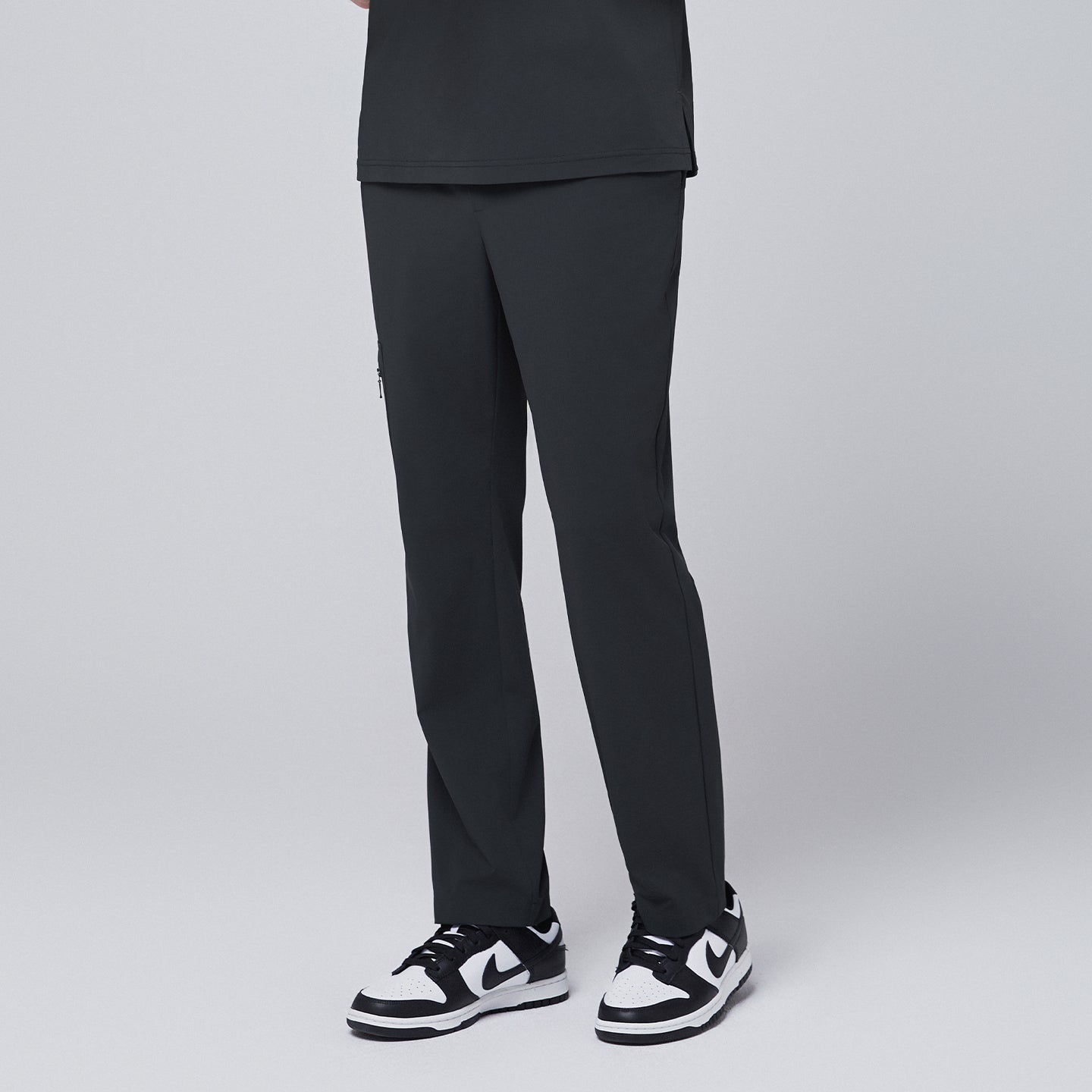 Side view of deep gray straight scrub pants showcasing a minimalist zipper pocket design, styled with black and white sneakers, modeled against a neutral gray backdrop,Deep Gray