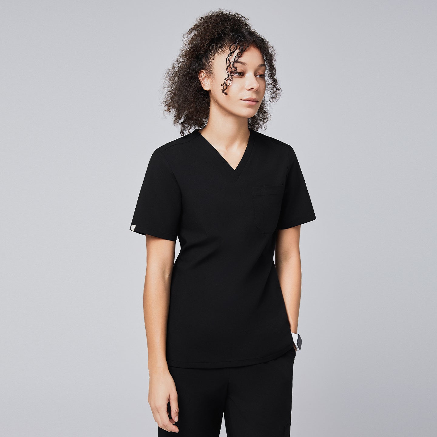 A woman wearing a black eco-friendly scrub top with a V-neck design and a chest pocket, styled with matching black scrub pants,Eco Black