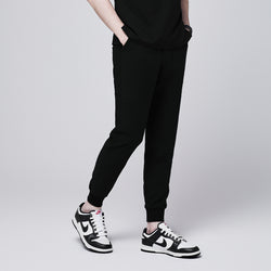 Image of Side view of black jogger scrub pants with 8 pockets, cuffed ankles, and hands in pockets, paired with black and white sneakers,Eco Black