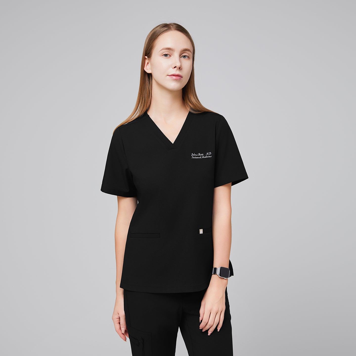 A woman wearing an Eco Black Double Pocket Scrub Top with a V-neck and short sleeves,Eco Black