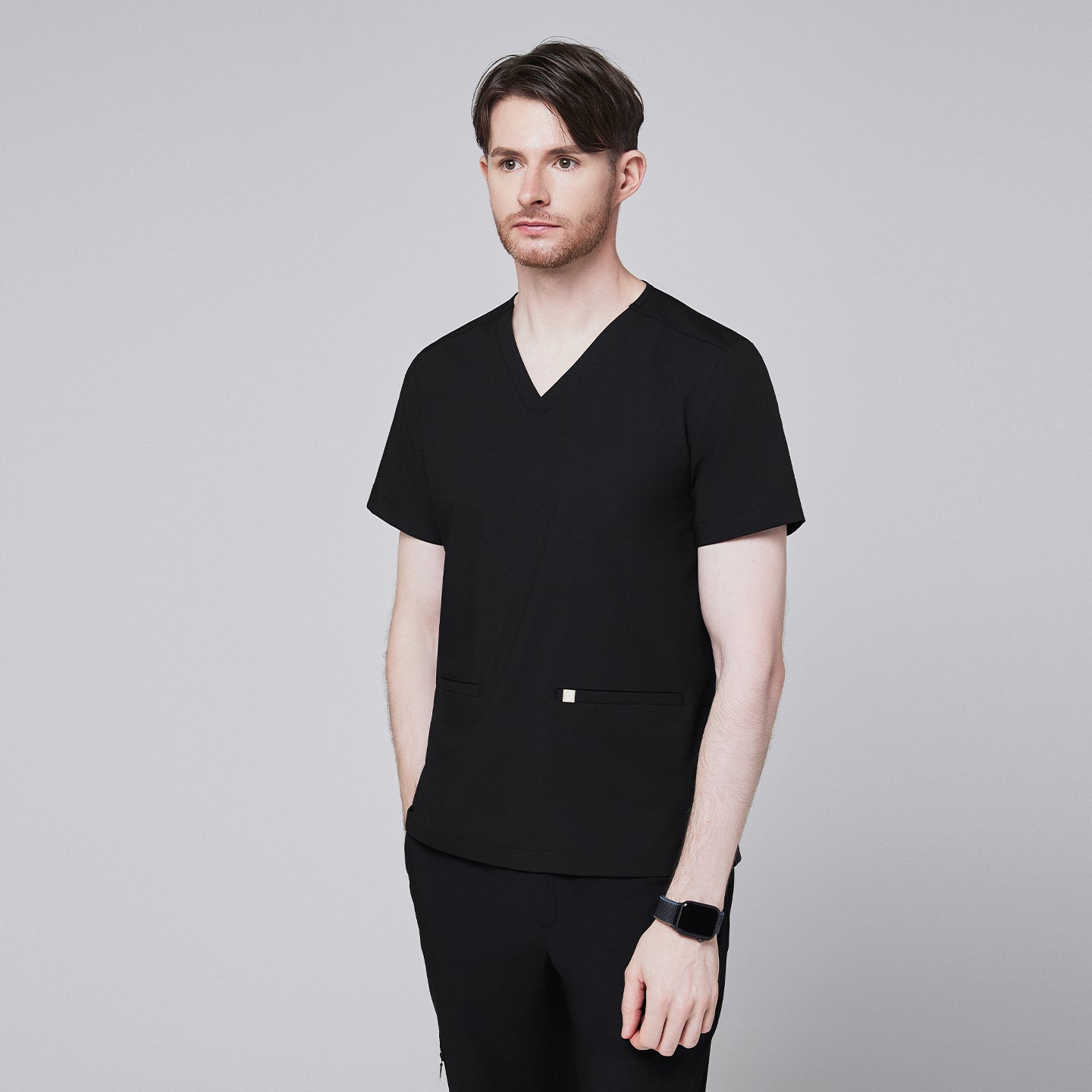 Man in black scrubs with a V-neck and double pockets, looking to the side with a thoughtful expression,Eco Black