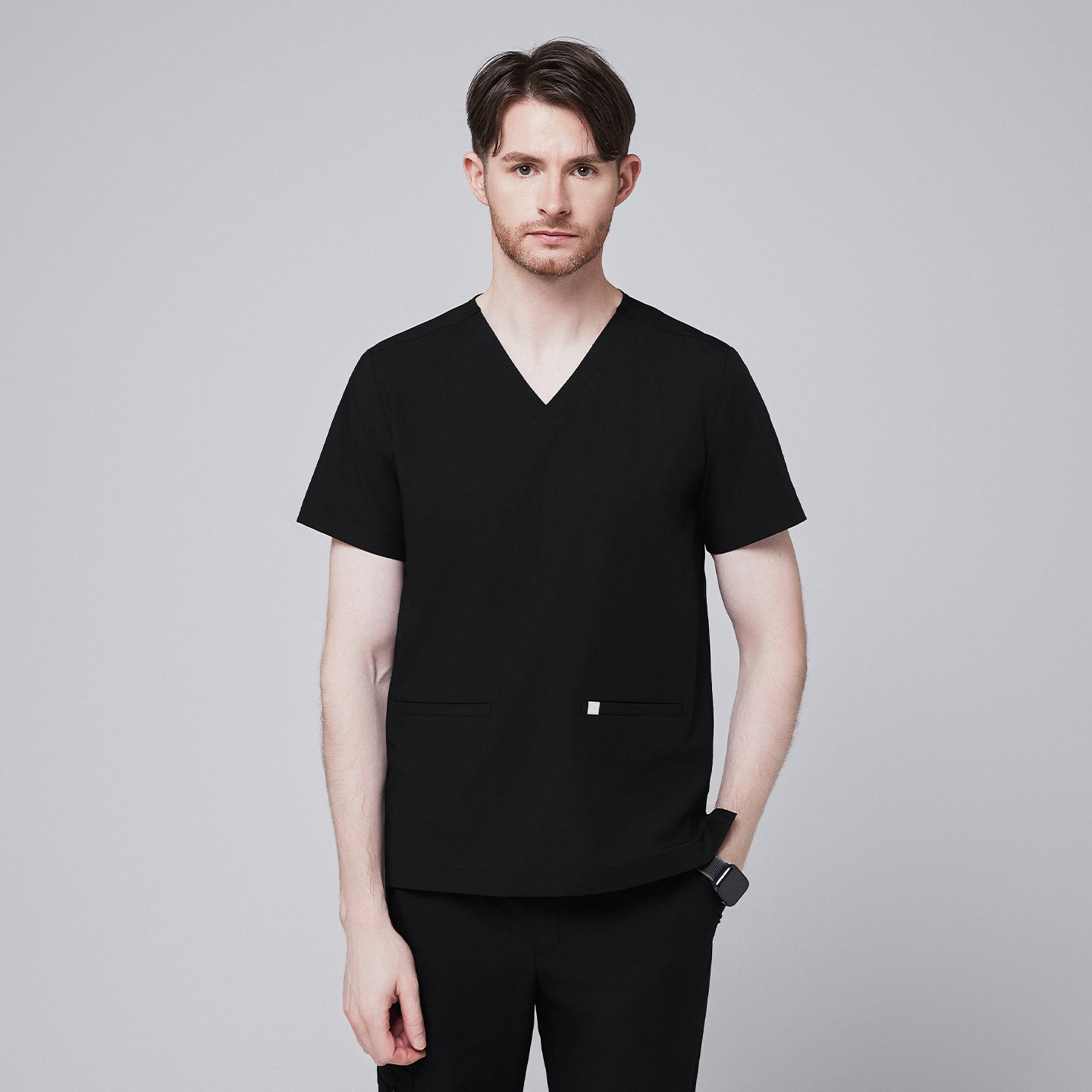 Man wearing black scrubs with a V-neck and double pockets, standing with a neutral expression,Eco Black