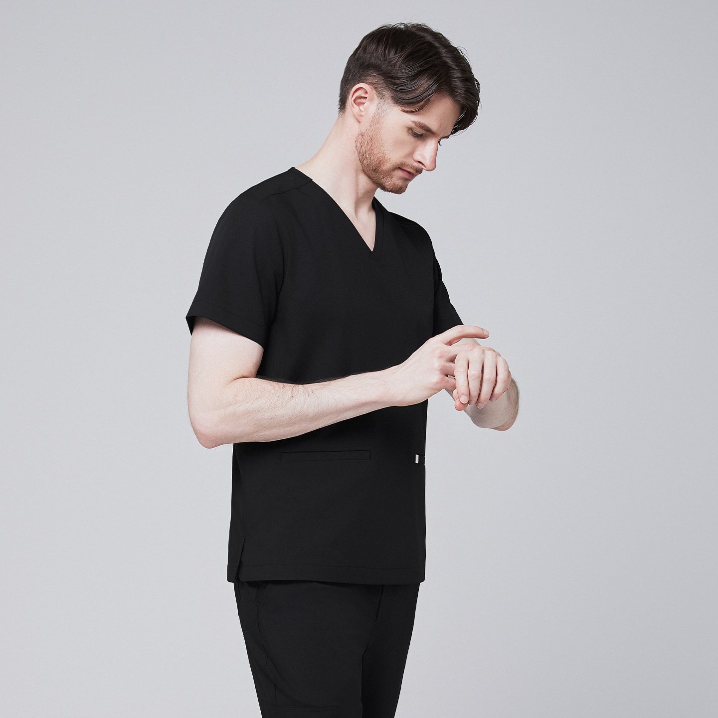 Man in black scrubs with a V-neck and double pockets, checking the time on his smartwatch,Eco Black