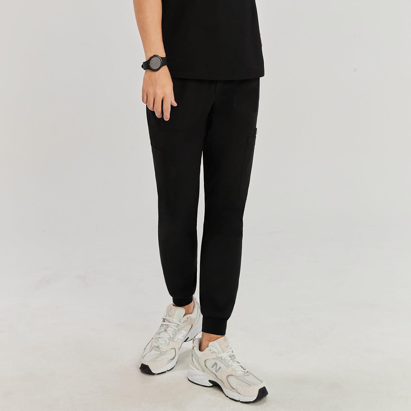 Model wearing jogger-style scrub pants with side pockets, shown in a relaxed stance with white sneakers.Eco Black