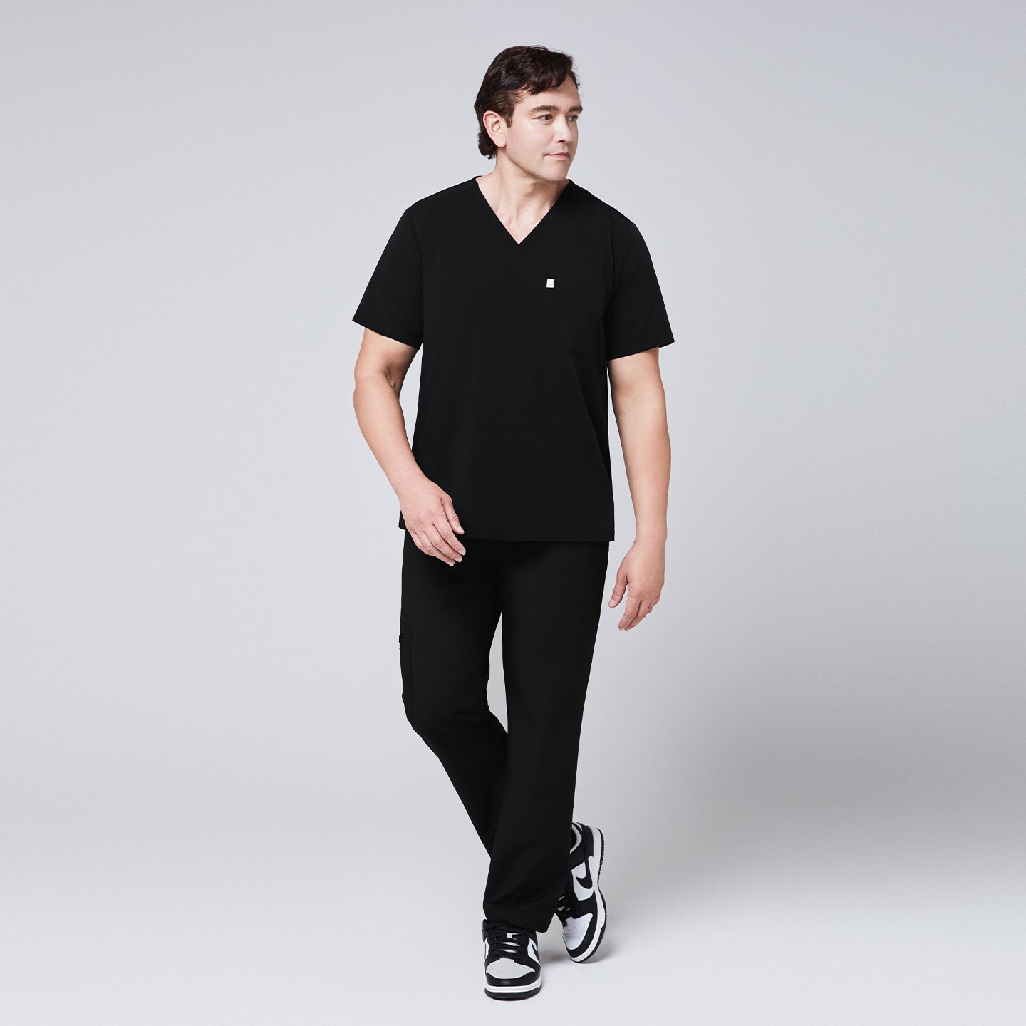 Full-body view of a man wearing a black scrub set with straight-leg pants and a single-pocket V-neck top,Eco Black