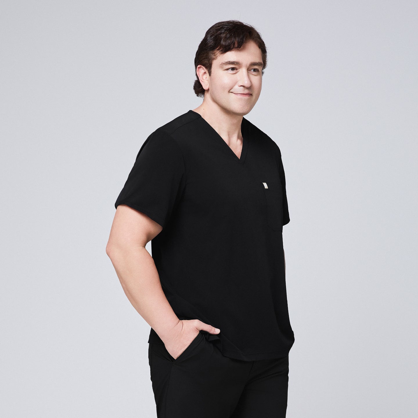 Man in a black scrub set with a single-pocket V-neck top, standing with one hand in his pocket,Eco Black