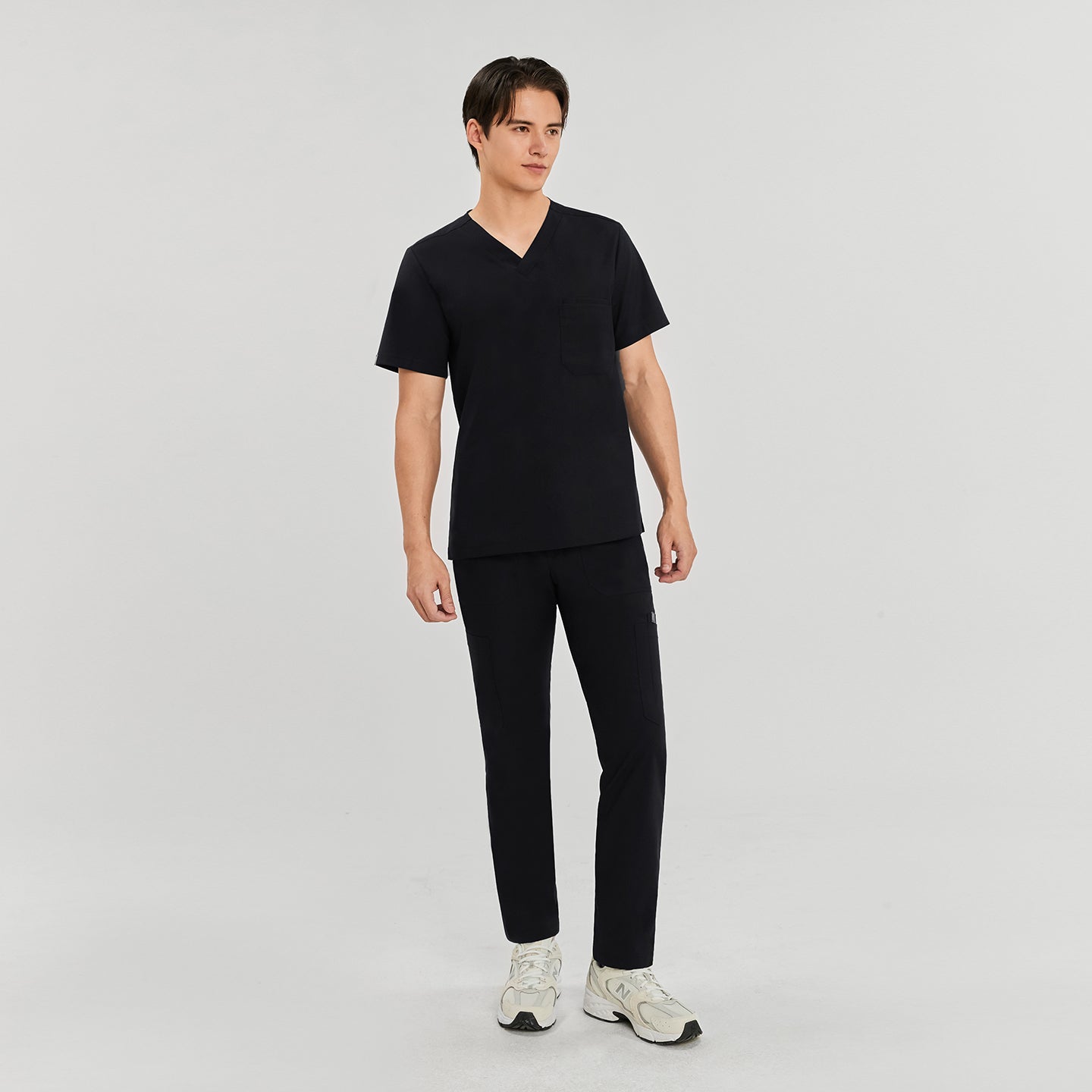 Man wearing zipper straight scrub pants with side pockets, a V-neck scrub top, and white New Balance sneakers,Eco Black