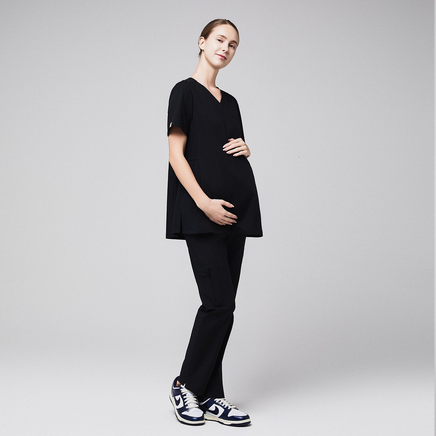 Pregnant healthcare professional in black maternity scrubs, holding her belly and standing confidently,Eco Black