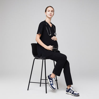 Pregnant healthcare professional in black maternity scrubs sitting on a stool, holding her belly with a stethoscope around her neck,Eco Black