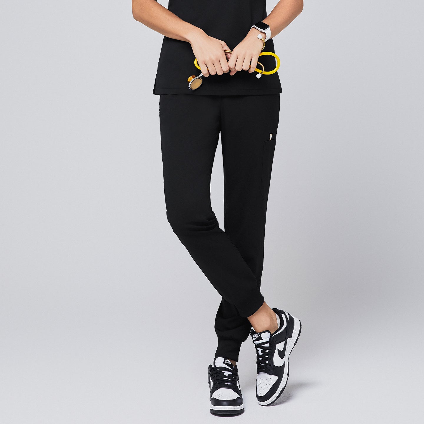 Black jogger scrub pants with a side pocket, elastic cuffs, and a clean design, paired with black-and-white sneakers and a yellow stethoscope,Eco Black