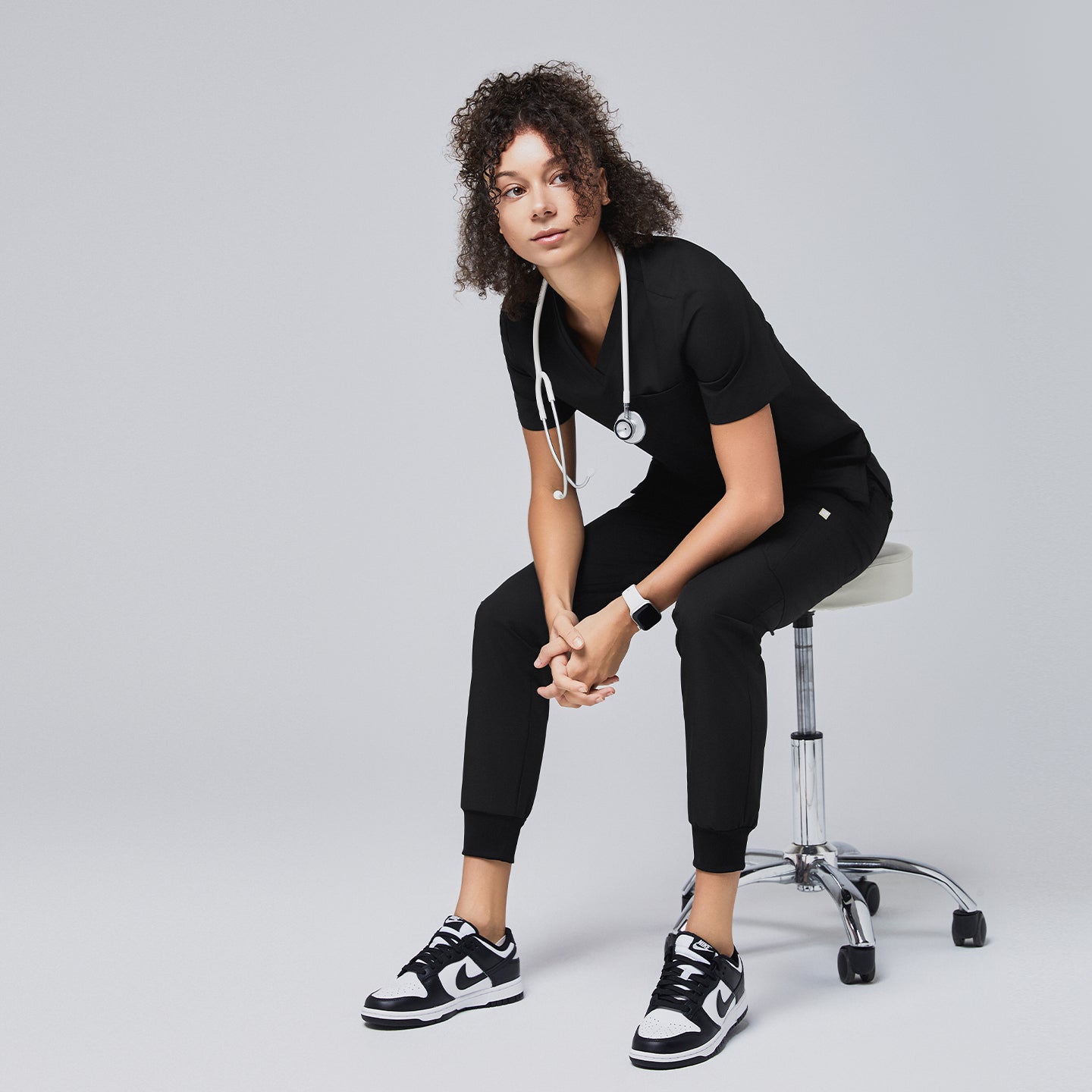 Professional scrub outfit featuring black jogger pants and matching top, styled for comfort and mobility while seated on a medical stool,Eco Black