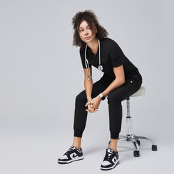 Image of Professional scrub outfit featuring black jogger pants and matching top, styled for comfort and mobility while seated on a medical stool,Eco Black