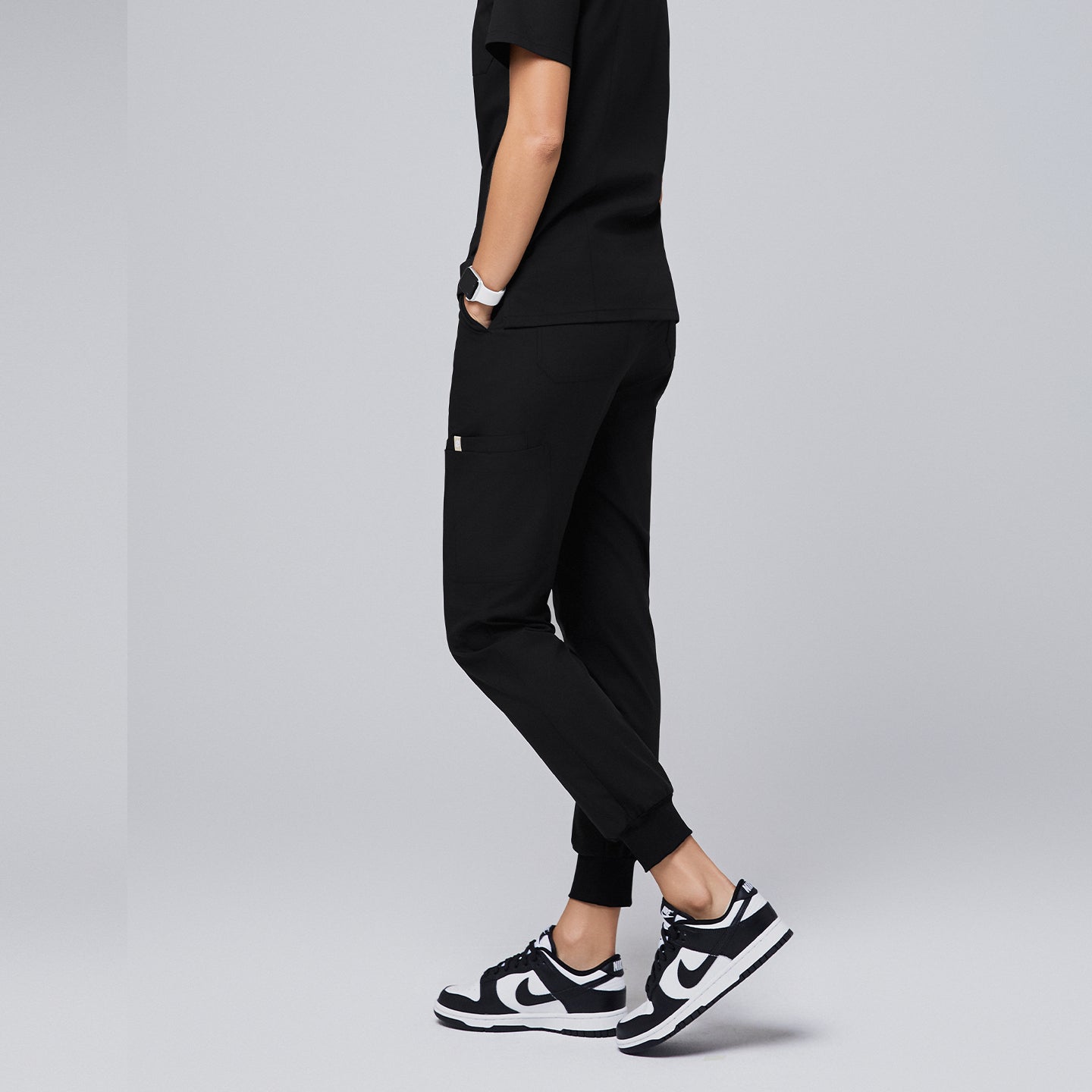 Black jogger scrub pants featuring a relaxed fit, side pockets, and cuffed ankles, paired with a matching top and black-and-white sneakers,Eco Black