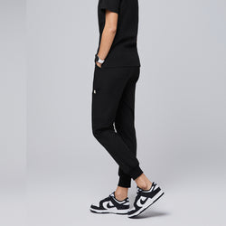 Image of Black jogger scrub pants featuring a relaxed fit, side pockets, and cuffed ankles, paired with a matching top and black-and-white sneakers,Eco Black