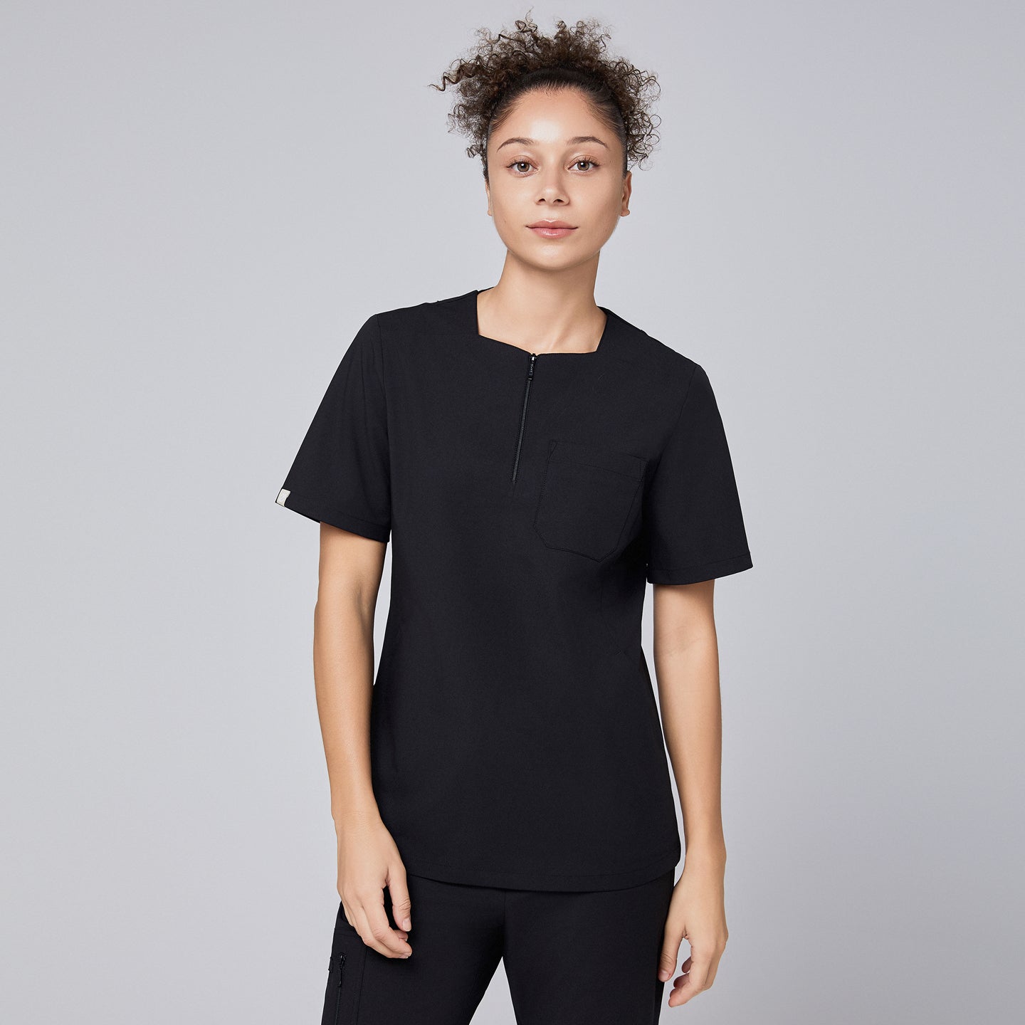 Model wearing an eco black scrub top with a quarter zipper, facing forward with a neutral expression,Eco Black