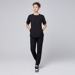 Image of Model wearing a black quarter-zip scrub set with a short-sleeve top featuring a chest pocket and matching jogger-style pants, paired with sneakers for a modern, professional look,Eco Black