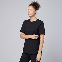 Image of Model wearing eco black scrub top with a quarter zipper, standing with one hand lightly holding the other arm, looking to the side,Eco Black