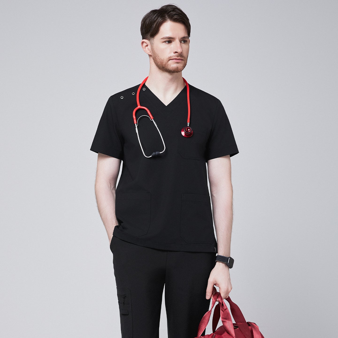 Man wearing Zenir black shoulder button scrub top with a red stethoscope and holding a red duffle bag,Eco Black