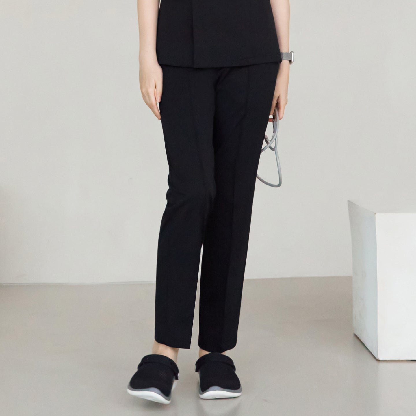 Front view of a woman wearing Eco Black W-Line Banding Scrub Pants with a matching top and black shoes, standing in a relaxed position,Eco Black