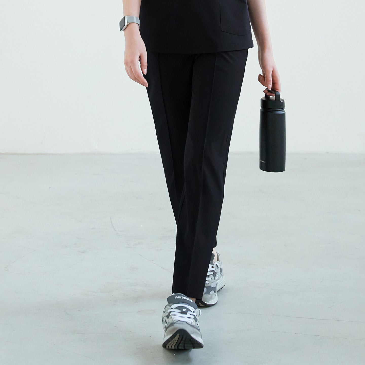 Black scrub pants with straight legs, paired with gray sneakers, shown in a walking pose while holding a black water bottle,Eco Black