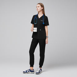 Image of Model wearing eco black jogger scrub pants with zipper pocket and matching scrub top, styled with a blue stethoscope and navy sneakers,Eco Black