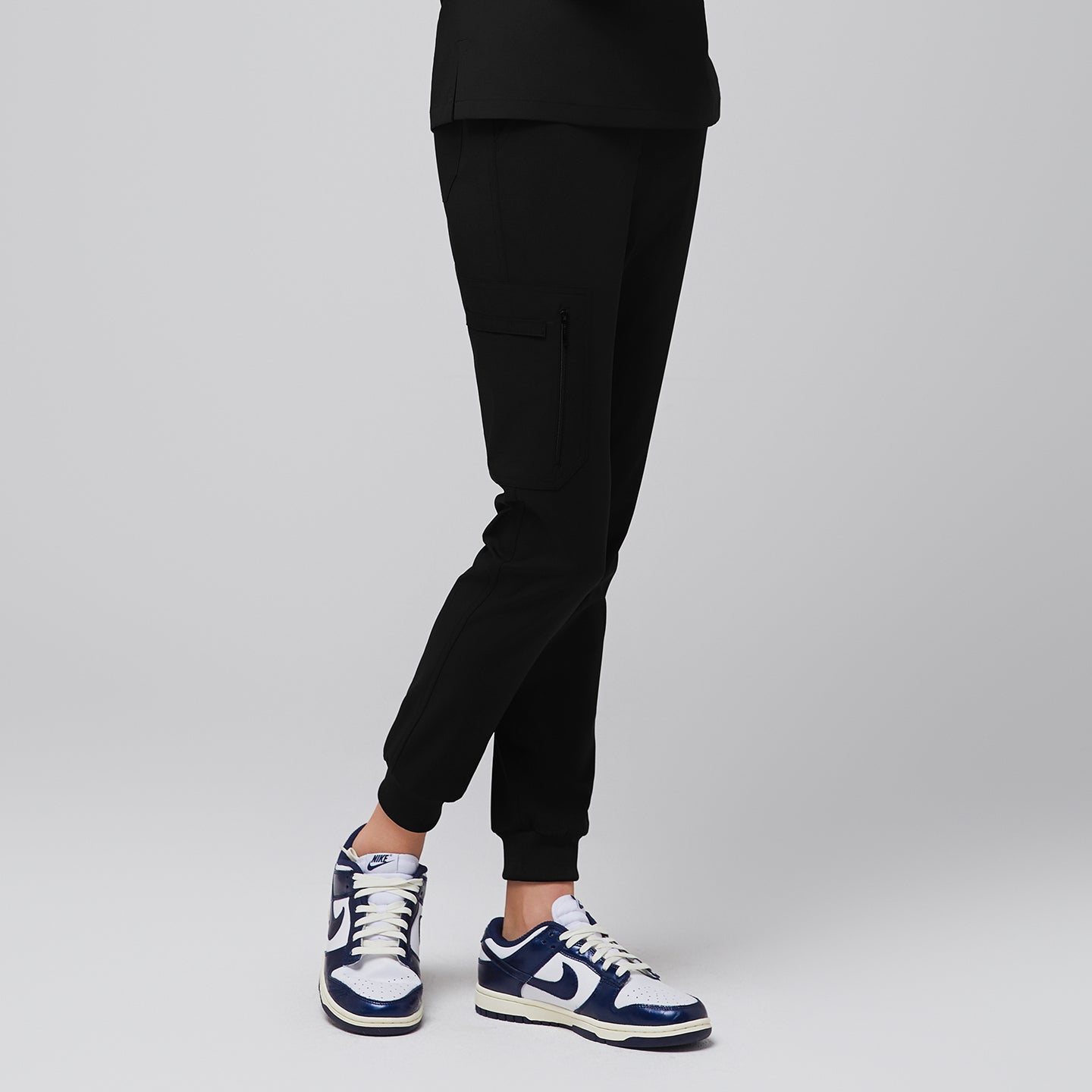 Side view of eco black jogger scrub pants with zipper pocket and elastic cuffs, paired with navy sneakers,Eco Black