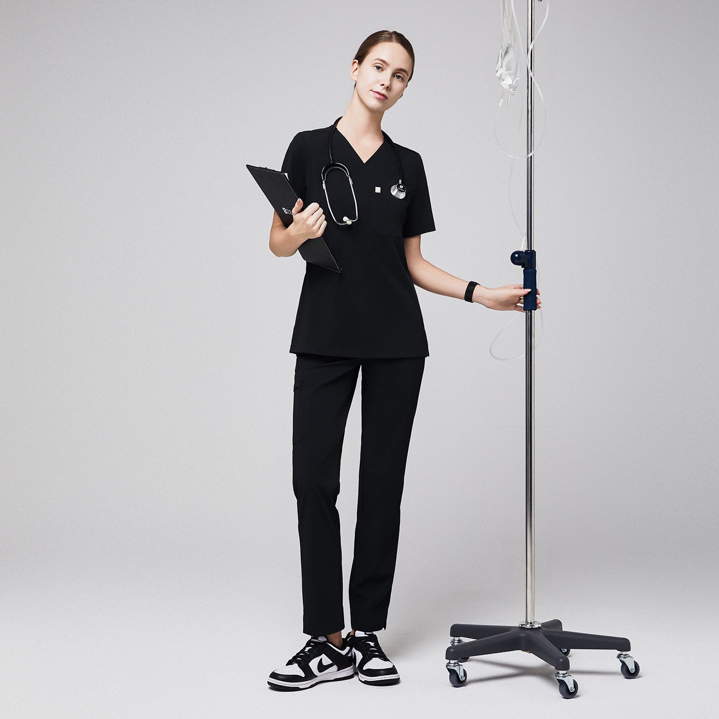 Medical professional in black scrub set with stethoscope and IV stand, featuring eco-friendly black scrub pants with zipper pocket and split hem,Eco Black