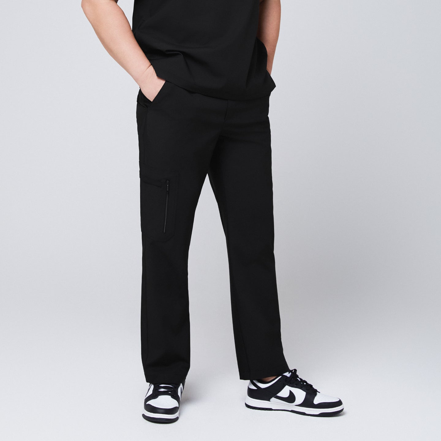 A male model wearing black straight scrub pants with a zipper pocket, paired with a matching scrub top and sneakers,Eco Black