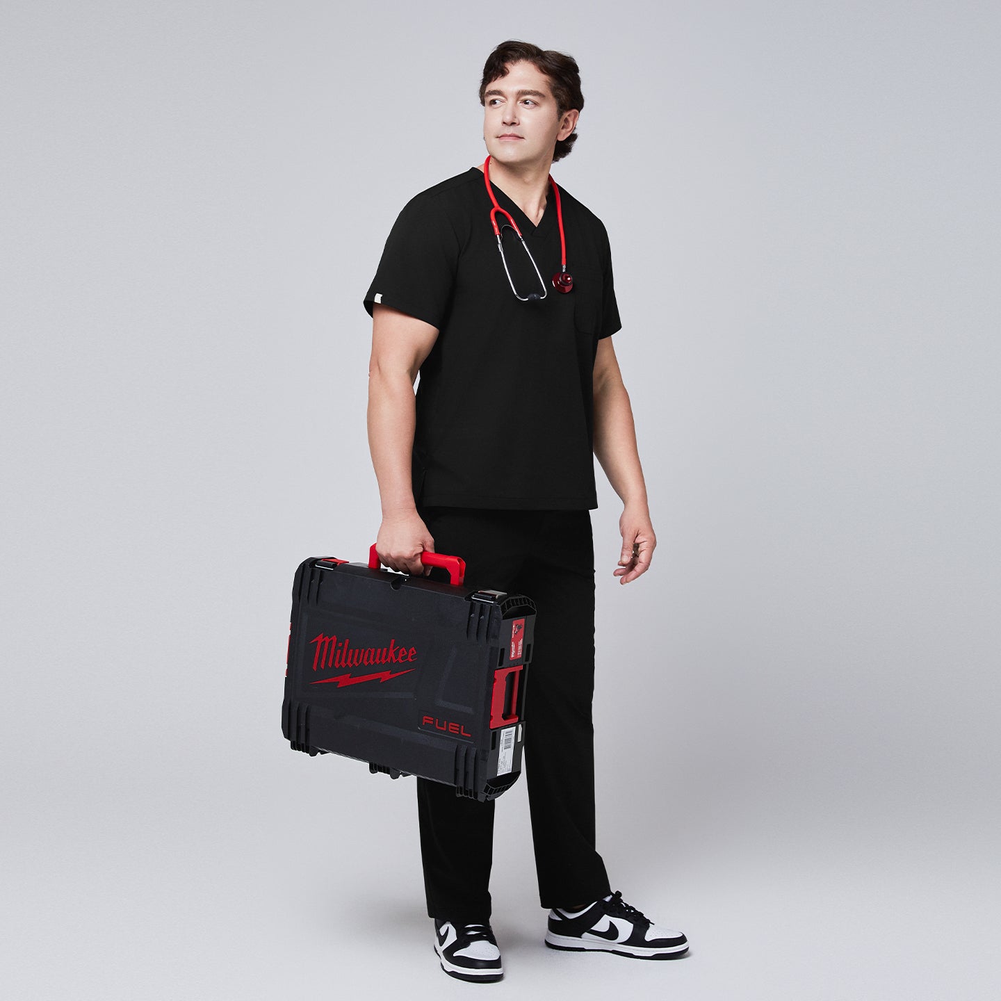 Male model in black scrub pants holding a Milwaukee Fuel case, styled with a stethoscope around his neck and sneakers,Eco Black