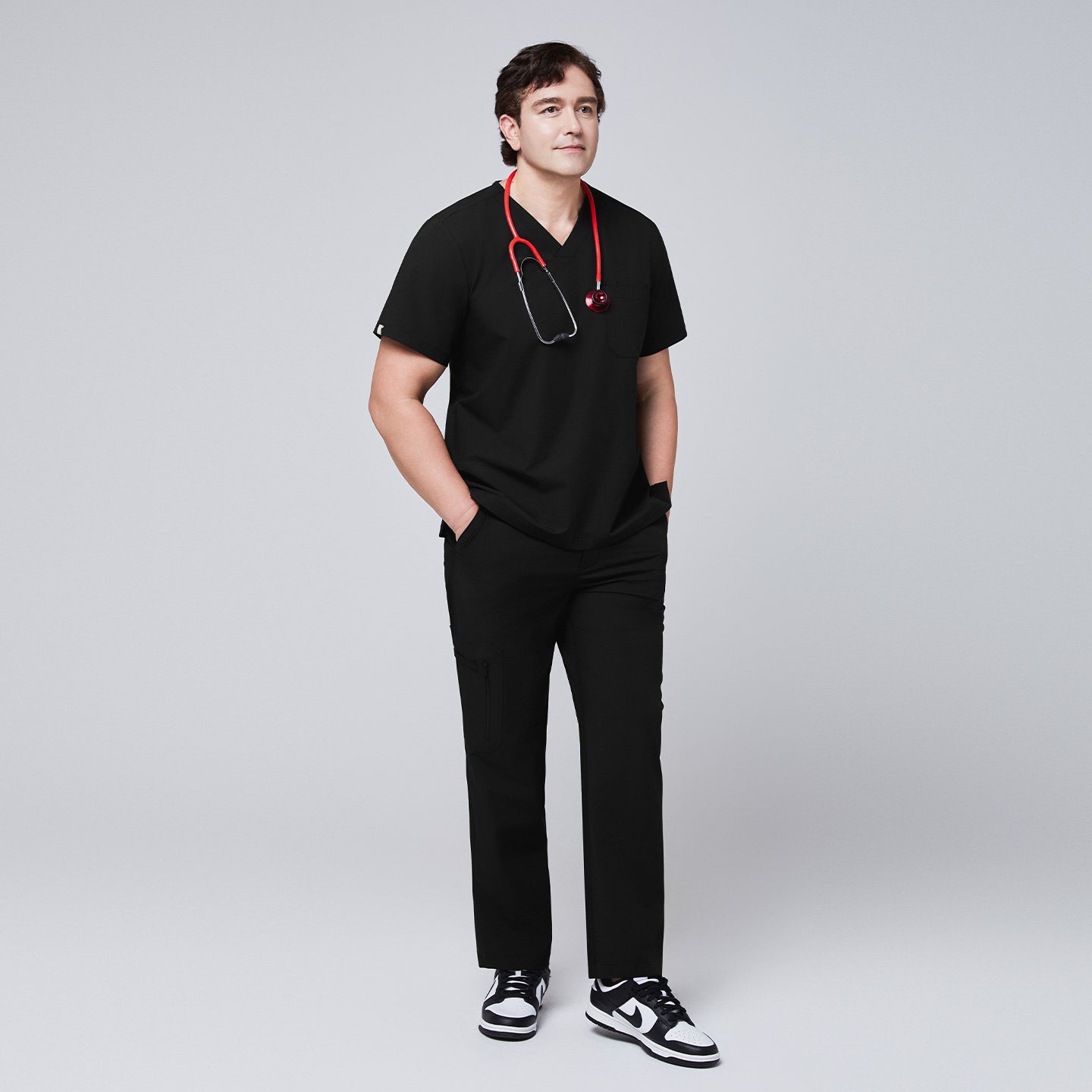 A male model in black straight scrub pants and a matching scrub top, accessorized with a red stethoscope and black sneakers, posing in a full-body shot,Eco Black