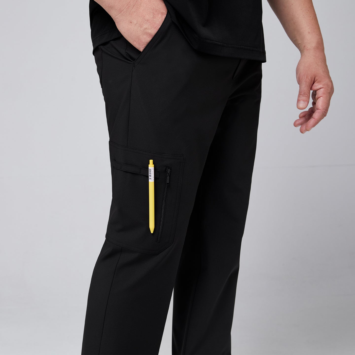 Male model wearing black straight scrub pants, highlighting the side zipper pocket with a yellow pen inserted,Eco Black