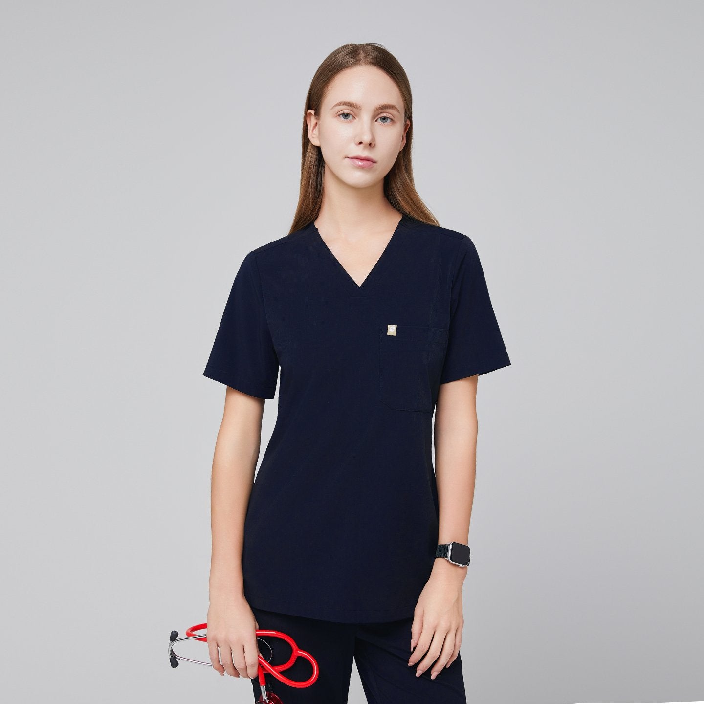 A woman wearing an Eco Navy Single Pocket Scrub Top with short sleeves, holding a red stethoscope,Eco Navy