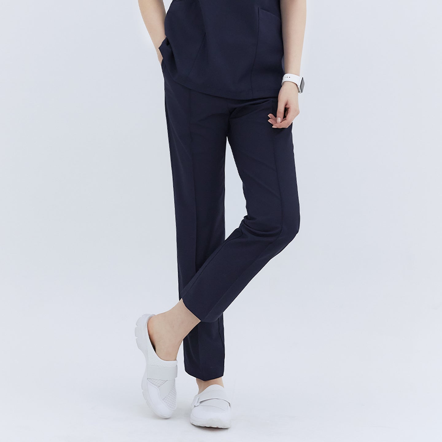  Front view of a woman wearing Eco Navy Line Banding Scrub Pants, highlighting the sleek design and pockets. She is standing with one leg crossed over the other, paired with white shoes,Eco Navy