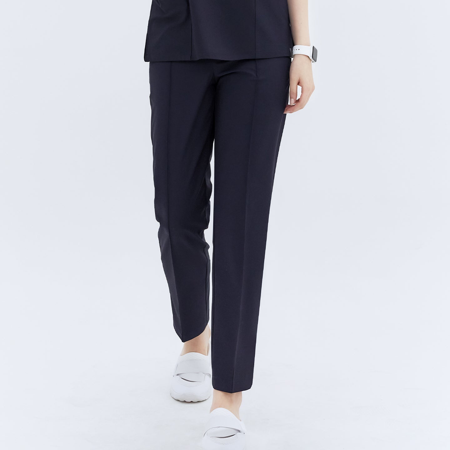 Close-up front view of a woman wearing Eco Navy Line Banding Scrub Pants, highlighting the sleek design and full length of the pants paired with white shoes,Eco Navy