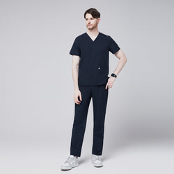 Image of Male model in a full-body pose wearing a navy V-neck scrub top with double front pockets and matching navy scrub pants, styled with casual sneakers, ideal for healthcare professionals,Eco Navy