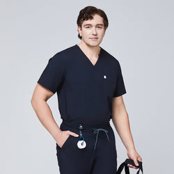 Image of Man wearing a navy scrub set with a single-pocket top, holding a black bag and accessorized with a retractable badge reel,Eco Navy