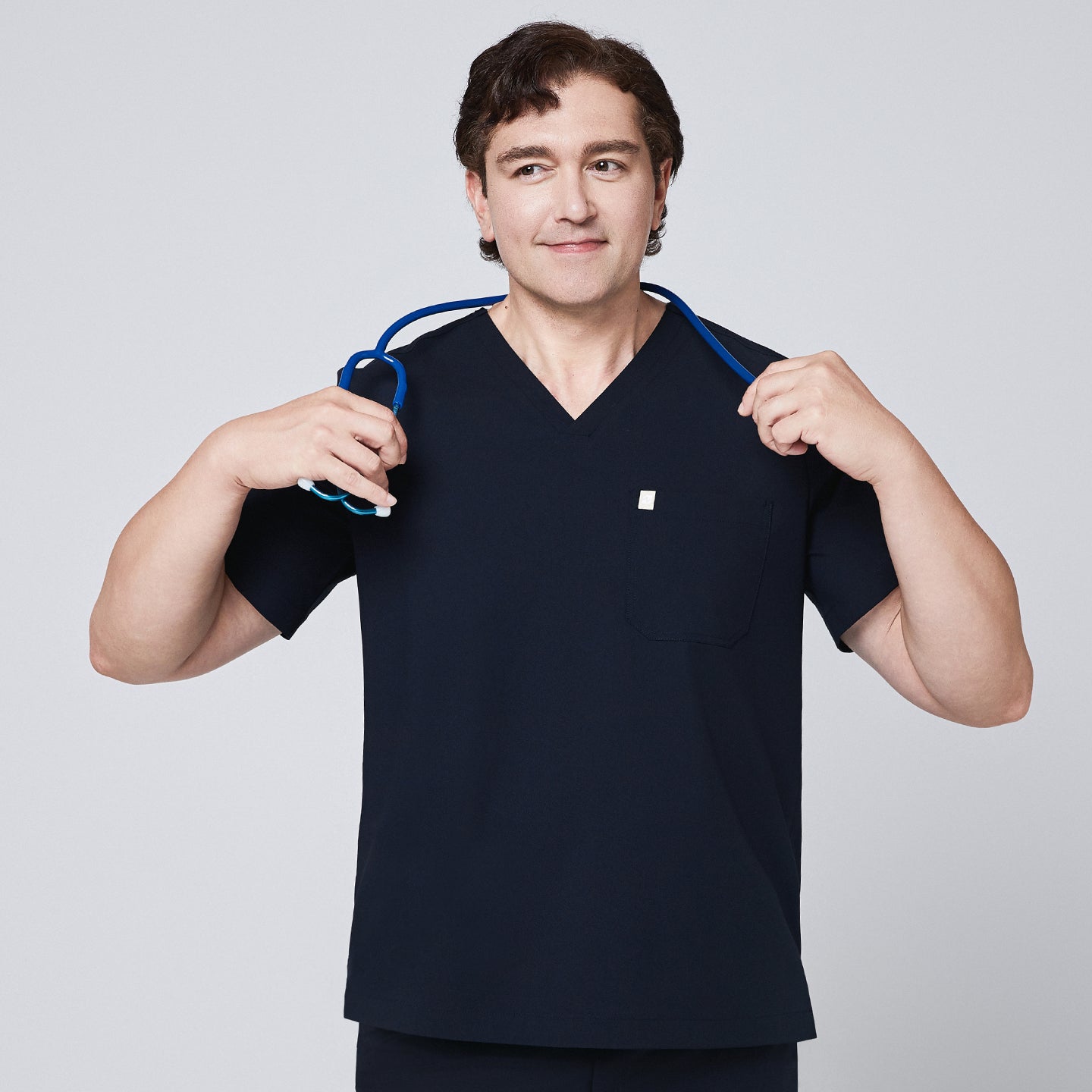 Male doctor in a navy scrub top with a single pocket, holding a blue stethoscope around his neck,Eco Navy