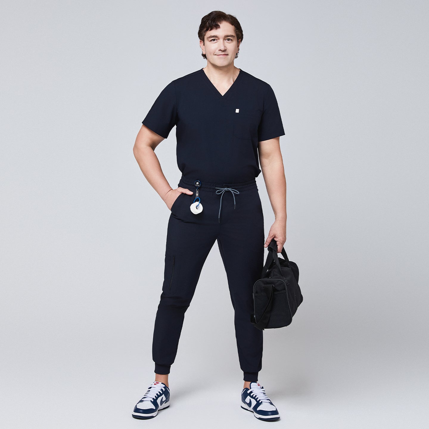 Male healthcare professional wearing a navy scrub set with jogger-style pants, holding a black medical bag,Eco Navy