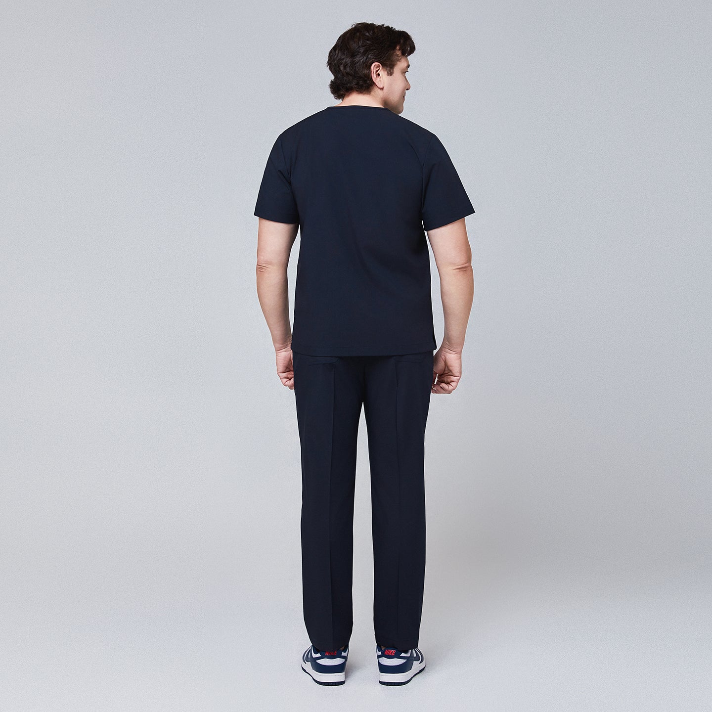 Back view of a man wearing a navy scrub set, featuring straight-leg pants and a short-sleeve top,Eco Navy