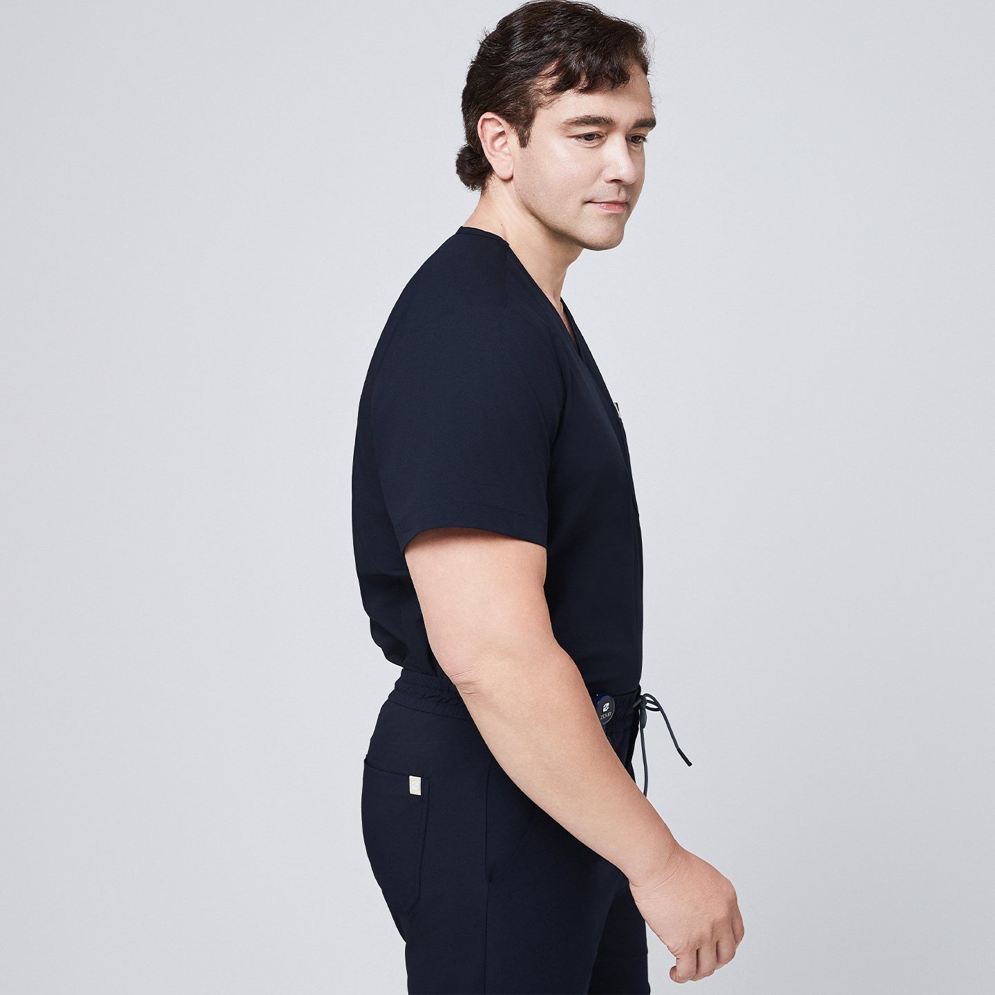 Side profile of model wearing navy scrub top and jogger scrub pants with a drawstring waist,Eco Navy