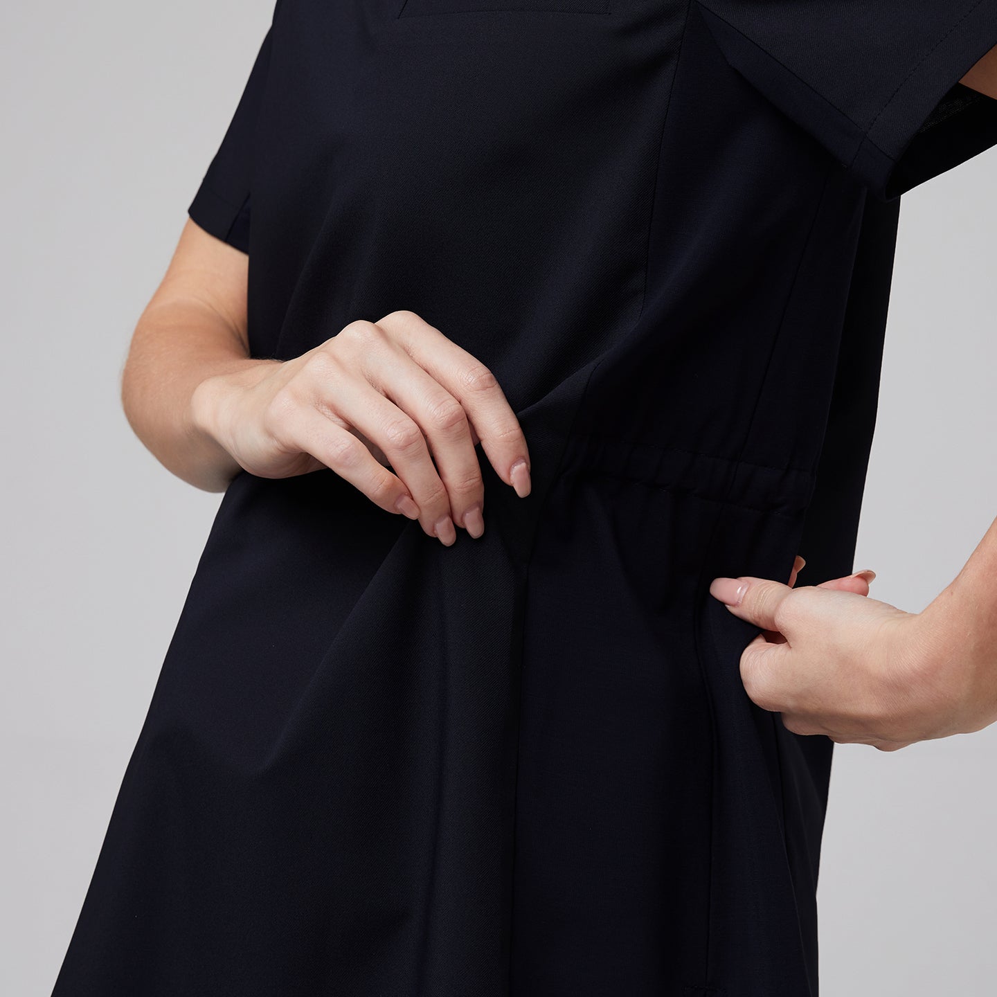 Hands adjusting the elastic side panel on a navy maternity scrub top, highlighting the adjustable and flexible design for comfort,Eco Navy