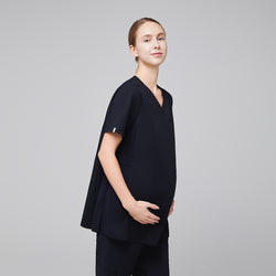 Image of Pregnant woman wearing navy maternity scrub top, shown in a side profile, gently cradling her belly, smiling confidently,Eco Navy