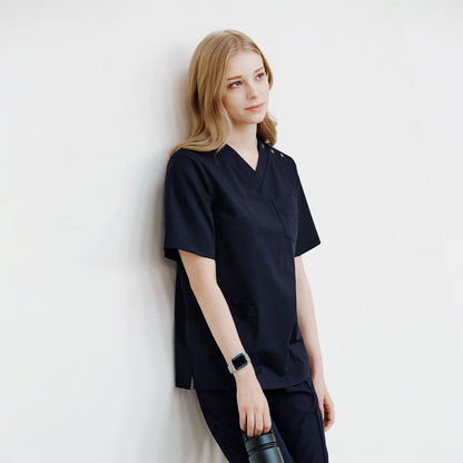 Half-side view of a woman leaning against a wall, wearing a navy scrub top and holding a water bottle,Eco Navy