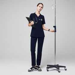 Image of Female healthcare professional in navy scrubs with zipper pocket pants, holding a clipboard and standing next to an IV stand,Eco Navy