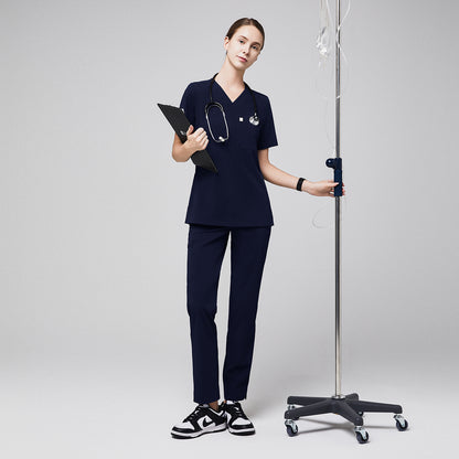 Female healthcare professional in navy scrubs with zipper pocket pants, holding a clipboard and standing next to an IV stand,Eco Navy