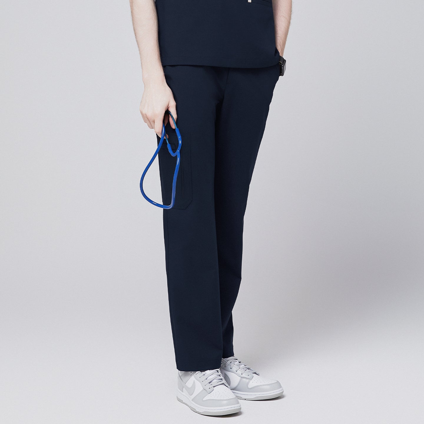 A model wearing navy straight scrub pants with a zipper pocket and matching scrub top, holding a blue stethoscope, paired with white sneakers,Eco Navy