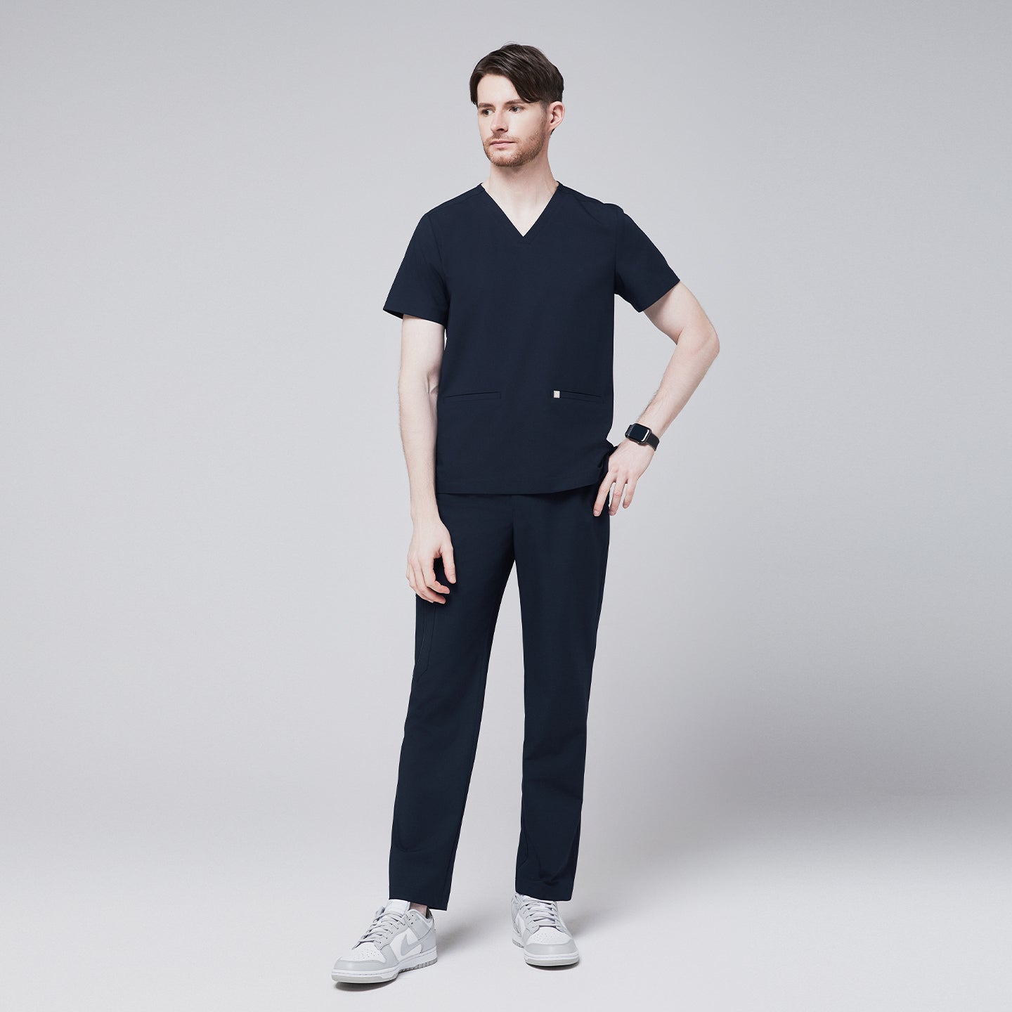 Full-body side view of a model wearing navy straight scrub pants with a zipper pocket and a matching scrub top, paired with white sneakers,Eco Navy