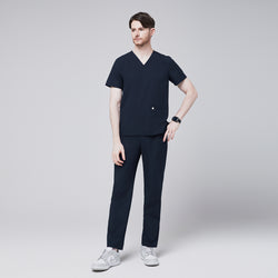 Image of Full-body side view of a model wearing navy straight scrub pants with a zipper pocket and a matching scrub top, paired with white sneakers,Eco Navy