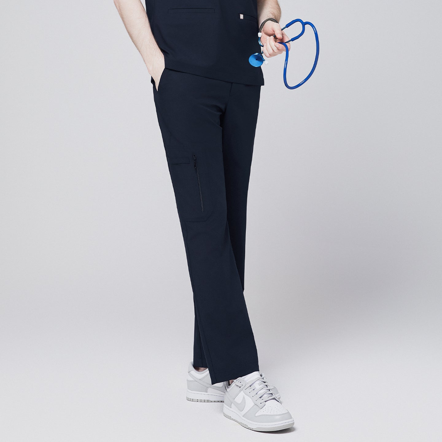 A model showcasing navy straight scrub pants with a zipper pocket and matching top, holding a blue stethoscope and styled with white sneakers,Eco Navy